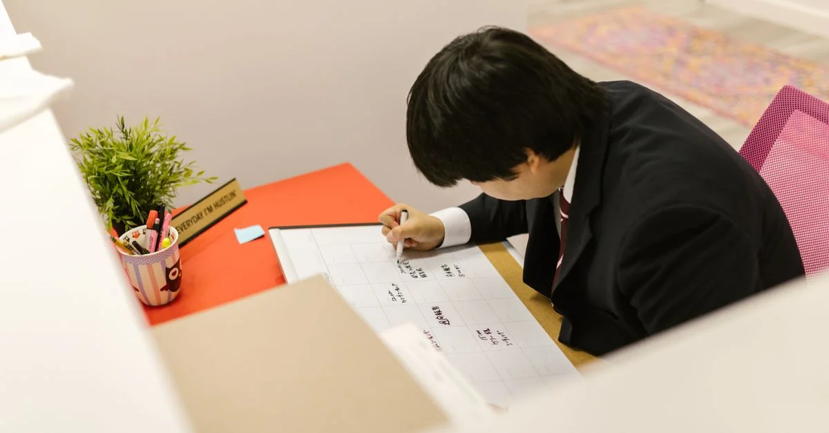 Profesional de negocios escribiendo en el calendario mensual en el escritorio de una oficina moderna.