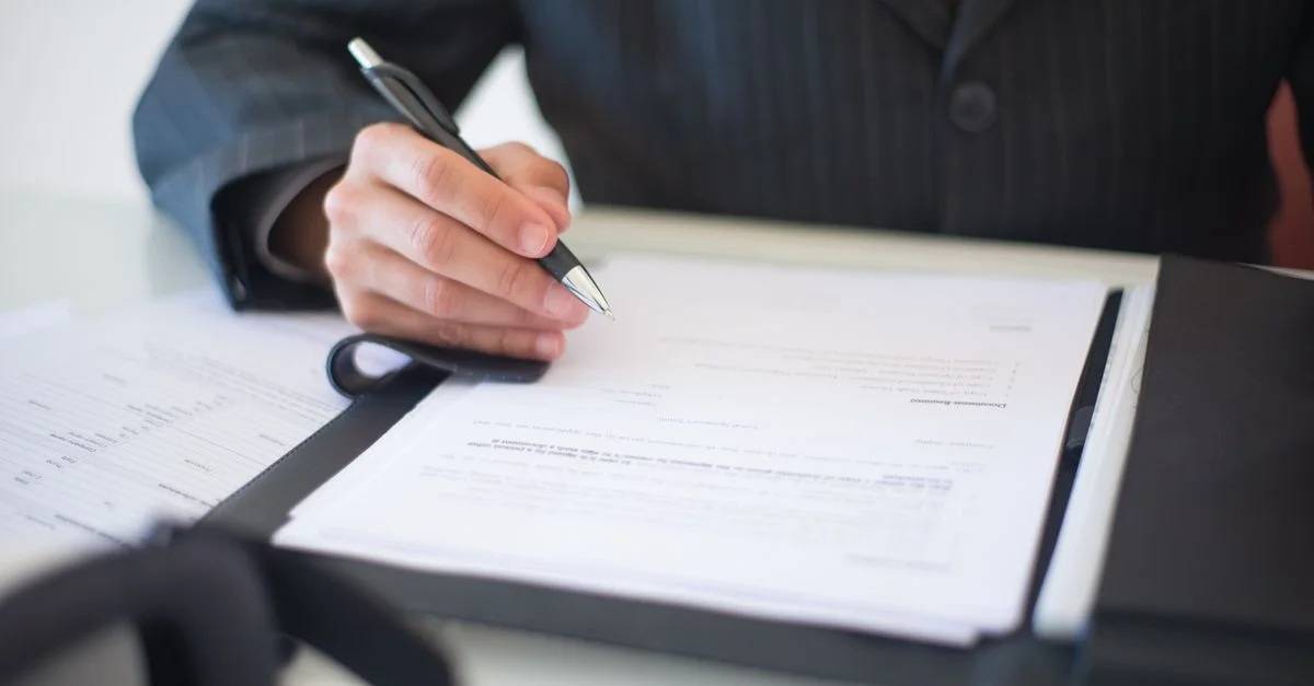 Primer plano de una mano firmando documentos con un bolígrafo, simbolizando un importante contrato empresarial.