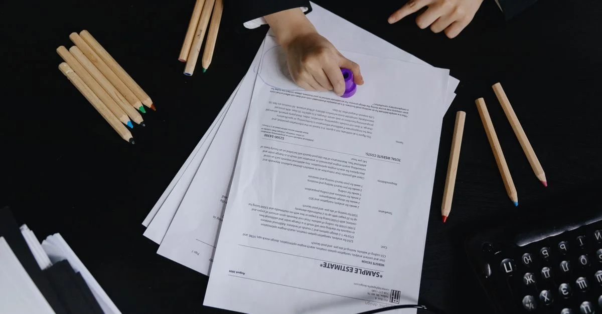Manos trabajando con documentos y lápices de colores en una vista de escritorio negro.