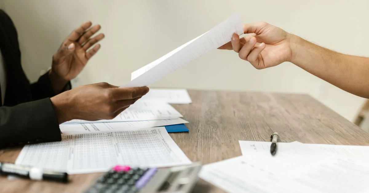 Dos profesionales intercambiando documentos en un entorno corporativo, enfatizando la colaboración y el trabajo administrativo.